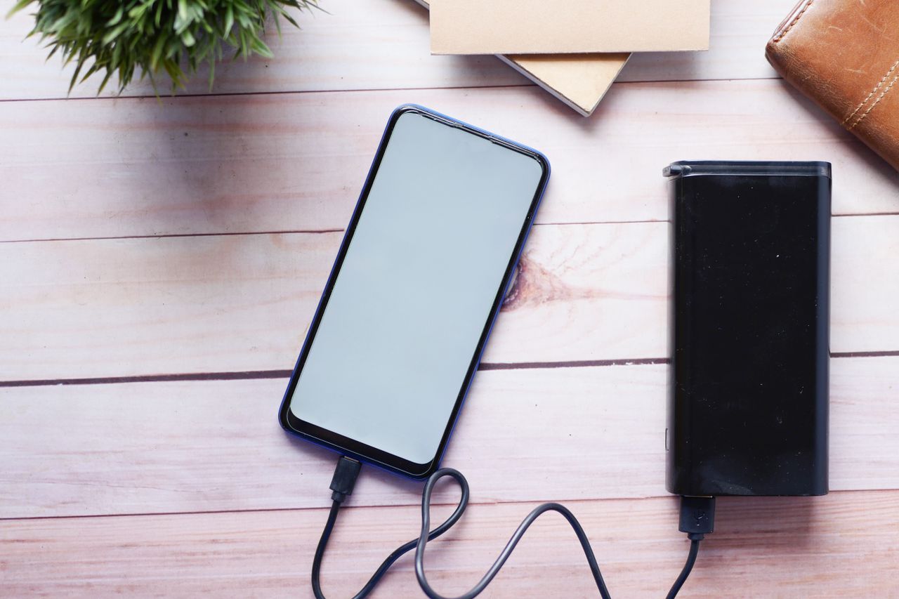 services-02 Smartphone charging with a power bank on a wooden desk, showcasing modern technology essentials.